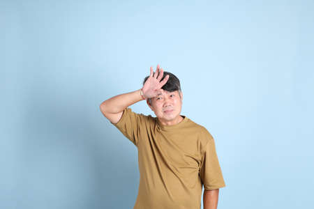 The senior Asian man with casual clothes standing on the blue background.