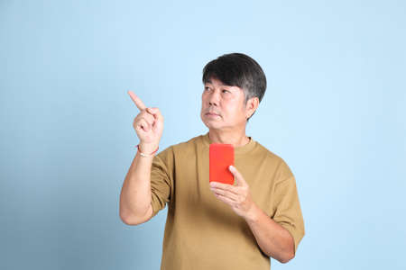 The senior Asian man with casual clothes standing on the blue background.
