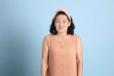The senior Asian woman with brown dressed standing on the blue background.の写真素材