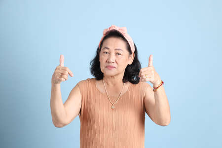 The senior Asian woman with brown dressed standing on the blue background.