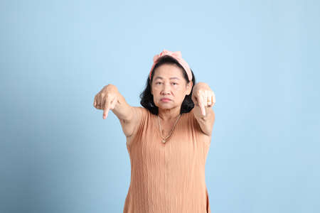 The senior Asian woman with brown dressed standing on the blue background.の写真素材