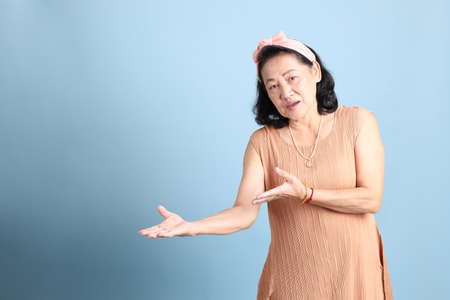 The senior Asian woman with brown dressed standing on the blue background.
