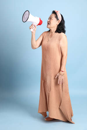 The senior Asian woman with brown dressed standing on the blue background.の写真素材