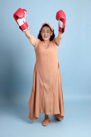 The senior Asian woman with brown dressed standing on the blue background.の写真素材