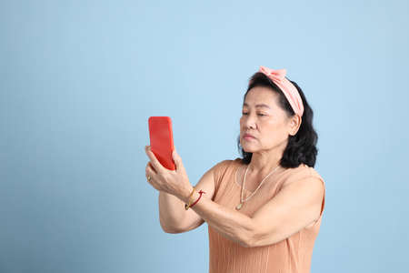 The senior Asian woman with brown dressed standing on the blue background.の写真素材