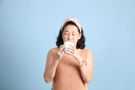 The senior Asian woman with brown dressed standing on the blue background.