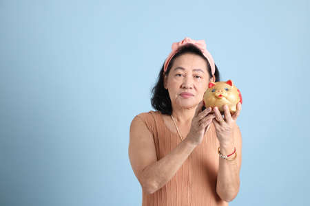 The senior Asian woman with brown dressed standing on the blue background.