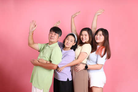 The happy Asian family standing on the pink background.