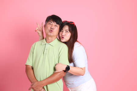The Asian father and daughter standing on the pink background.の写真素材