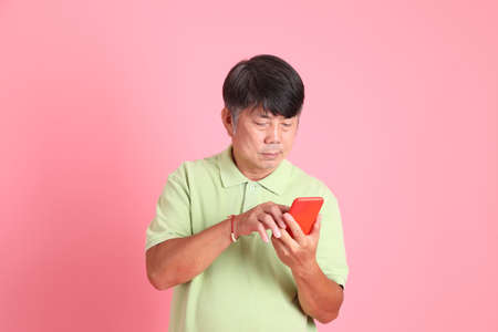 The senior Asian man with casual clothes standing on the pink background.の写真素材