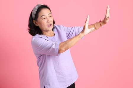 The senior Asian woman with brown dressed standing on the Pink background.