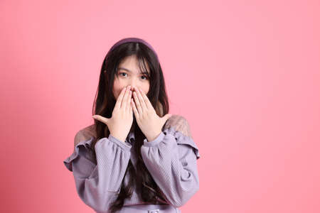 The cute young Asian woman with preppy dressed standing on the pink background.