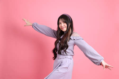 The cute young Asian woman with preppy dressed standing on the pink background.