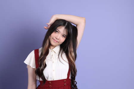 The cute young Asian woman with preppy dressed standing on the purple background.