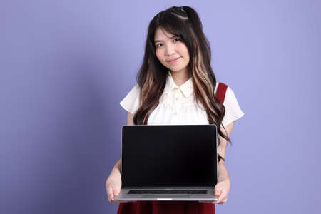 The cute young Asian woman with preppy dressed standing on the purple background.