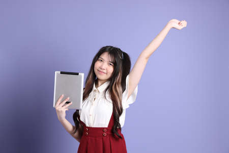 The cute young Asian woman with preppy dressed standing on the purple background.の写真素材