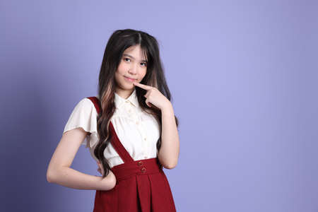 The cute young Asian woman with preppy dressed standing on the purple background.