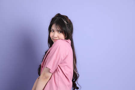 The cute young Asian girl with casual clothes standing on the purple background.