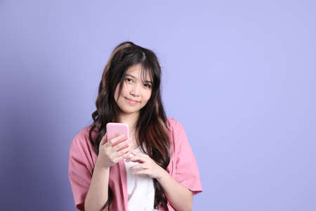 The cute young Asian girl with casual clothes standing on the purple background.