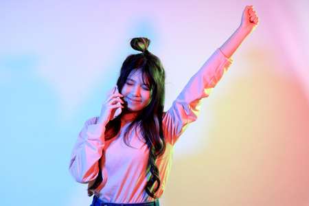 The cute young Asian girl with casual clothes posing under the gel color lightning in studio.