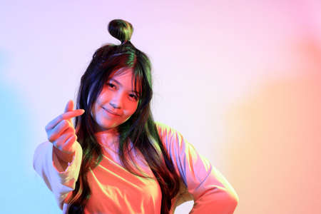 The cute young Asian girl with casual clothes posing under the gel color lightning in studio.