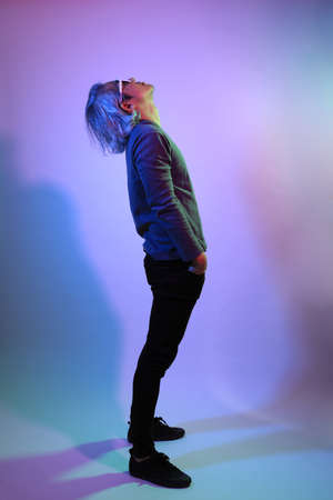 The cool senior Asian man standing on the white background under the color gel lighting.