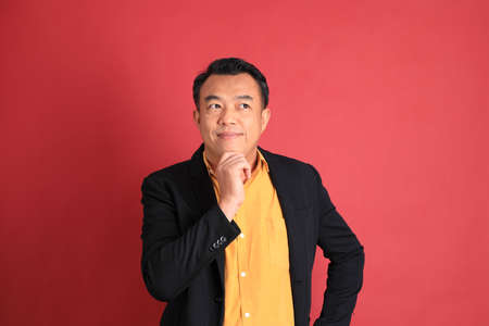 The Asian middle aged man standing on the red background.