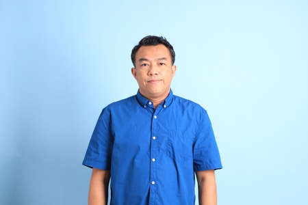 The Asian middle aged man with blue shirt standing on the blue background.の写真素材