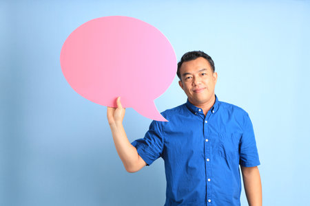 The Asian middle aged man with blue shirt standing on the blue background.