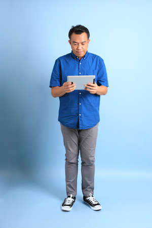 The Asian middle aged man with blue shirt standing on the blue background.の写真素材