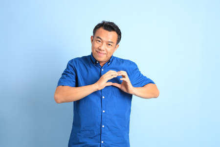 The Asian middle aged man with blue shirt standing on the blue background.