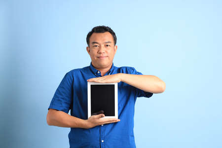 The Asian middle aged man with blue shirt standing on the blue background.