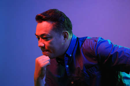 The cool senior Asian man on the blue background under the color gel lighting.