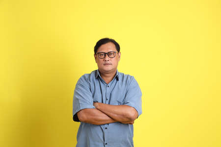 The adult Asian man with blue shirt standing on the yellow background.