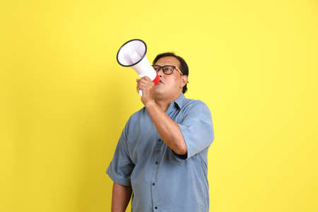 The adult Asian man with blue shirt standing on the yellow background.の写真素材