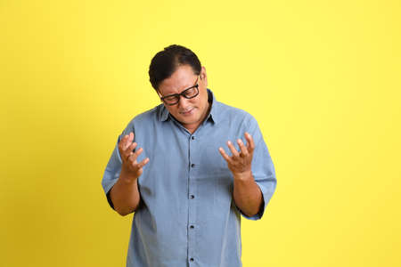 The adult Asian man with blue shirt standing on the yellow background.
