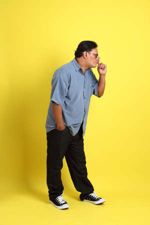 The adult Asian man with blue shirt standing on the yellow background.