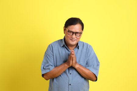 The adult Asian man with blue shirt standing on the yellow background.