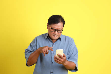 The adult Asian man with blue shirt standing on the yellow background.