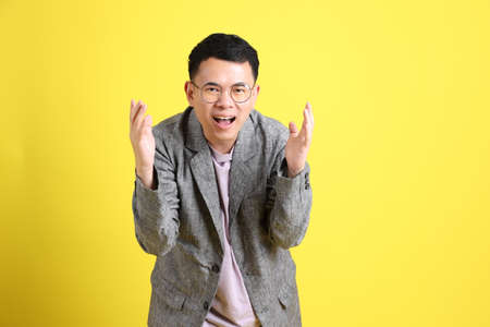 The Asian LGBTQ man with grey blazer standing on the yellow background.