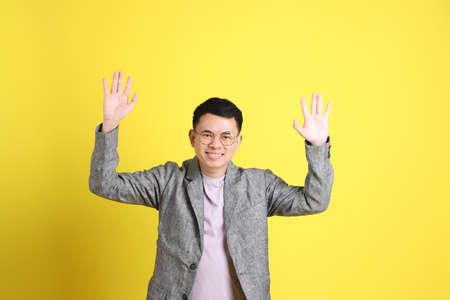 The Asian LGBTQ man with grey blazer standing on the yellow background.