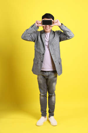 The Asian LGBTQ man with grey blazer standing on the yellow background.