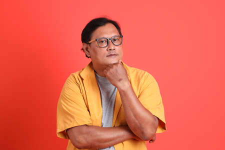 The adult Asian man with yellow shirt standing on the orange background.の写真素材