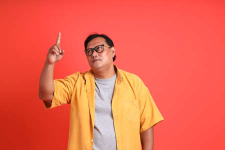 The adult Asian man with yellow shirt standing on the orange background.