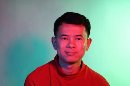 The cool adult Asian man on the blue background under the color gel lighting.