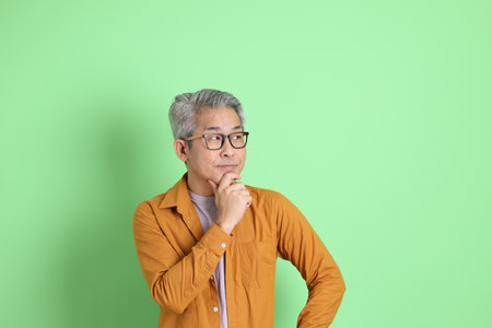 The 40s adult Asian man with yellow shirt standing on the green background.