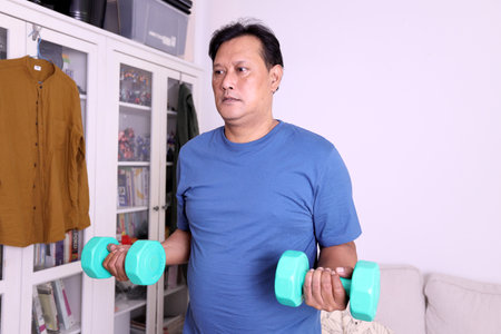 The 40s adult overweight Asian man lifting weight to work out at home.