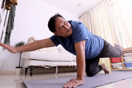 The 40s adult overweight Asian man watching exercise program on television and doing yoga on the map in the living room.の写真素材