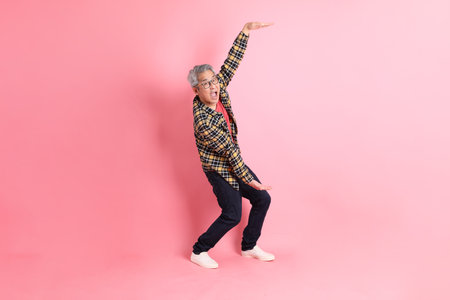 The full length of senior Asian man standing on the pink background.の写真素材