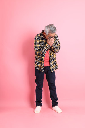 The full length of senior Asian man standing on the pink background.の写真素材